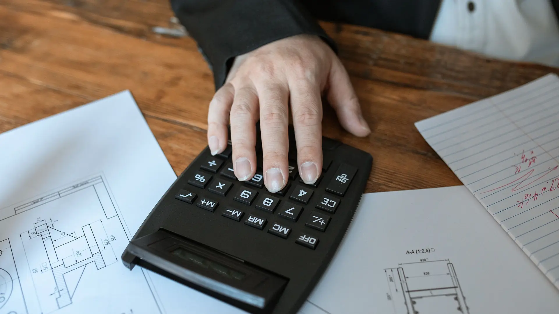 A hand using a calculator on top of house plans