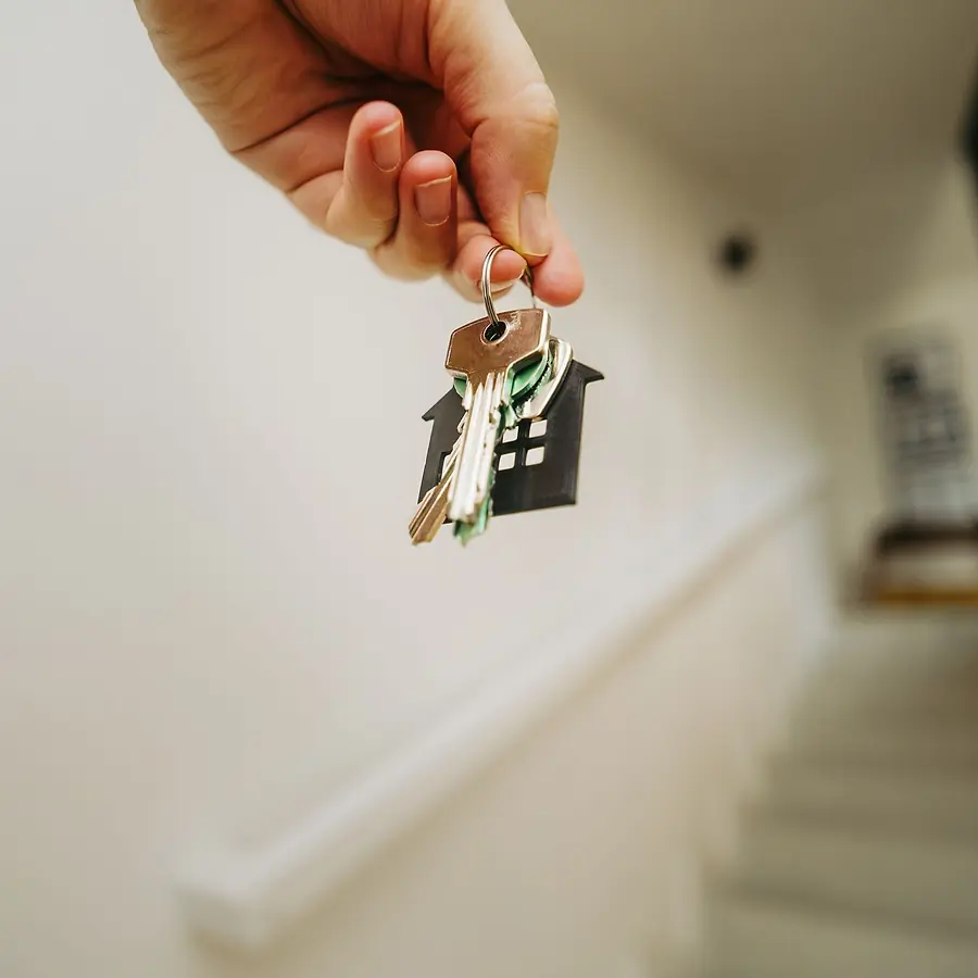 A hand holding house keys on a house-shaped key ring