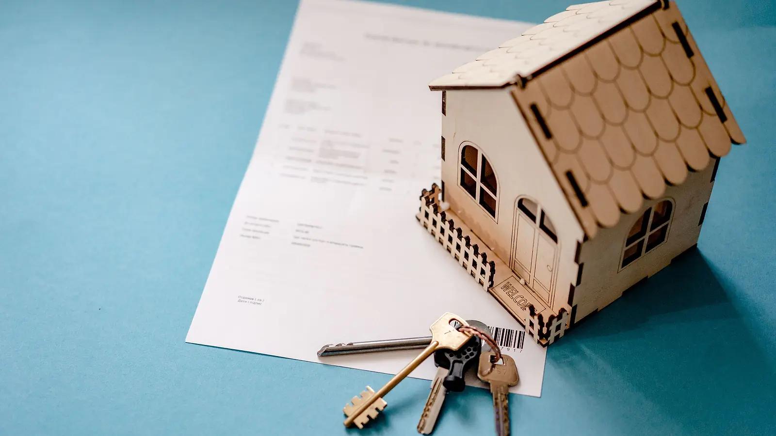 A small wooden model house with keys on top of a contract