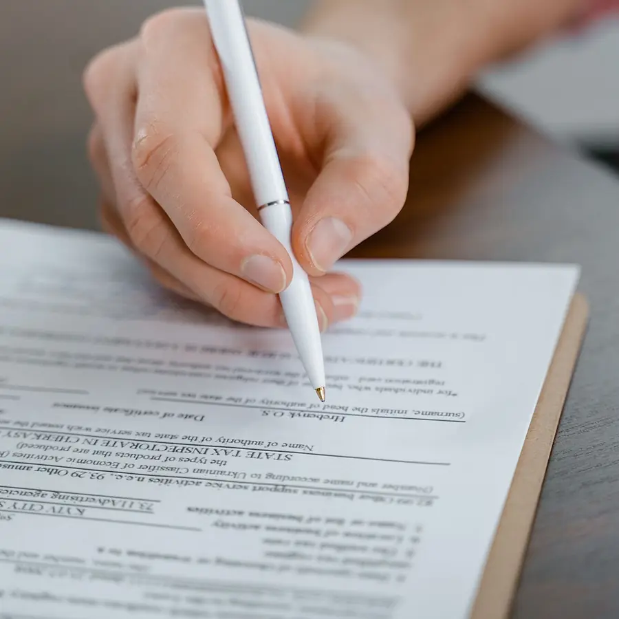 A hand signing a document with a pen